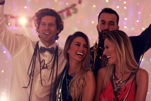 Group of friends enjoying a festive party, dressed elegantly with vibrant decorations, smiling and laughing under twinkling string lights - Mia Ishaaq