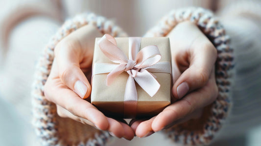 Close up of a models hands holding a ribbon tied gift box, models hands are in a heart shape position - Mia Ishaaq