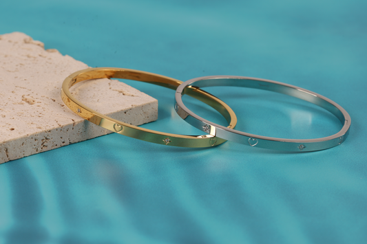 Gold and silver bangle bracelet placed against each other and leaning over a natural stone prop on the blue lagoon background making it look like they are floating on the water - Mia Ishaaq