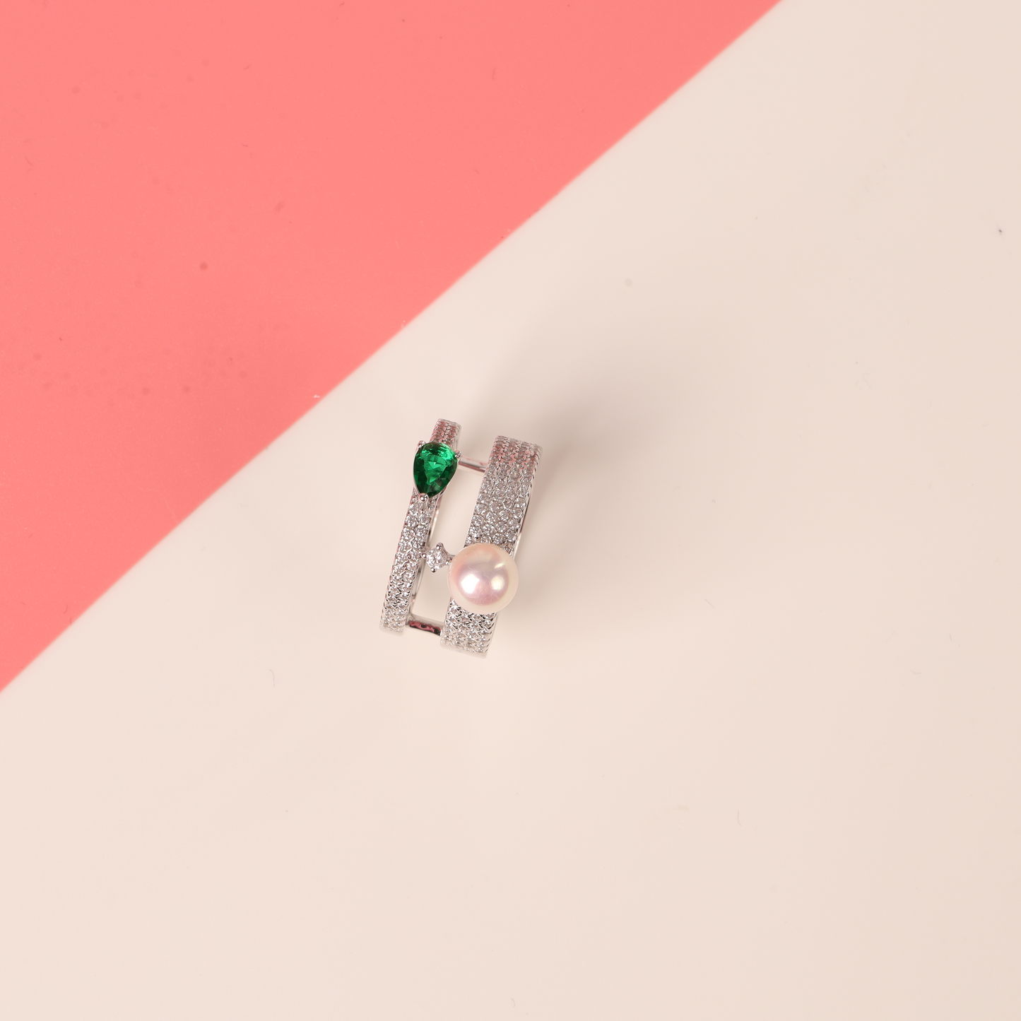 The Mia Ishaaq Green Cubic Zirconia Pearl Ring rests elegantly on a pink and cream background.