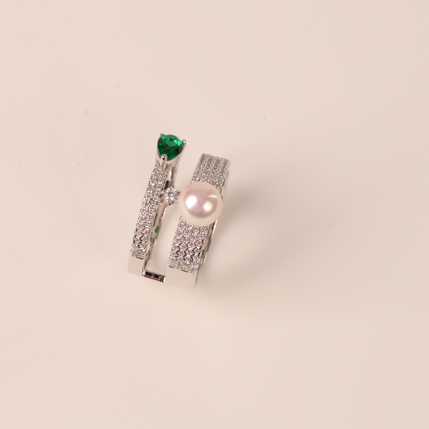 Mia Ishaaq's Green Cubic Zirconia Pearl Ring is crafted from sterling silver, showcasing a lustrous pearl and enhanced with small diamonds against a light pink backdrop.