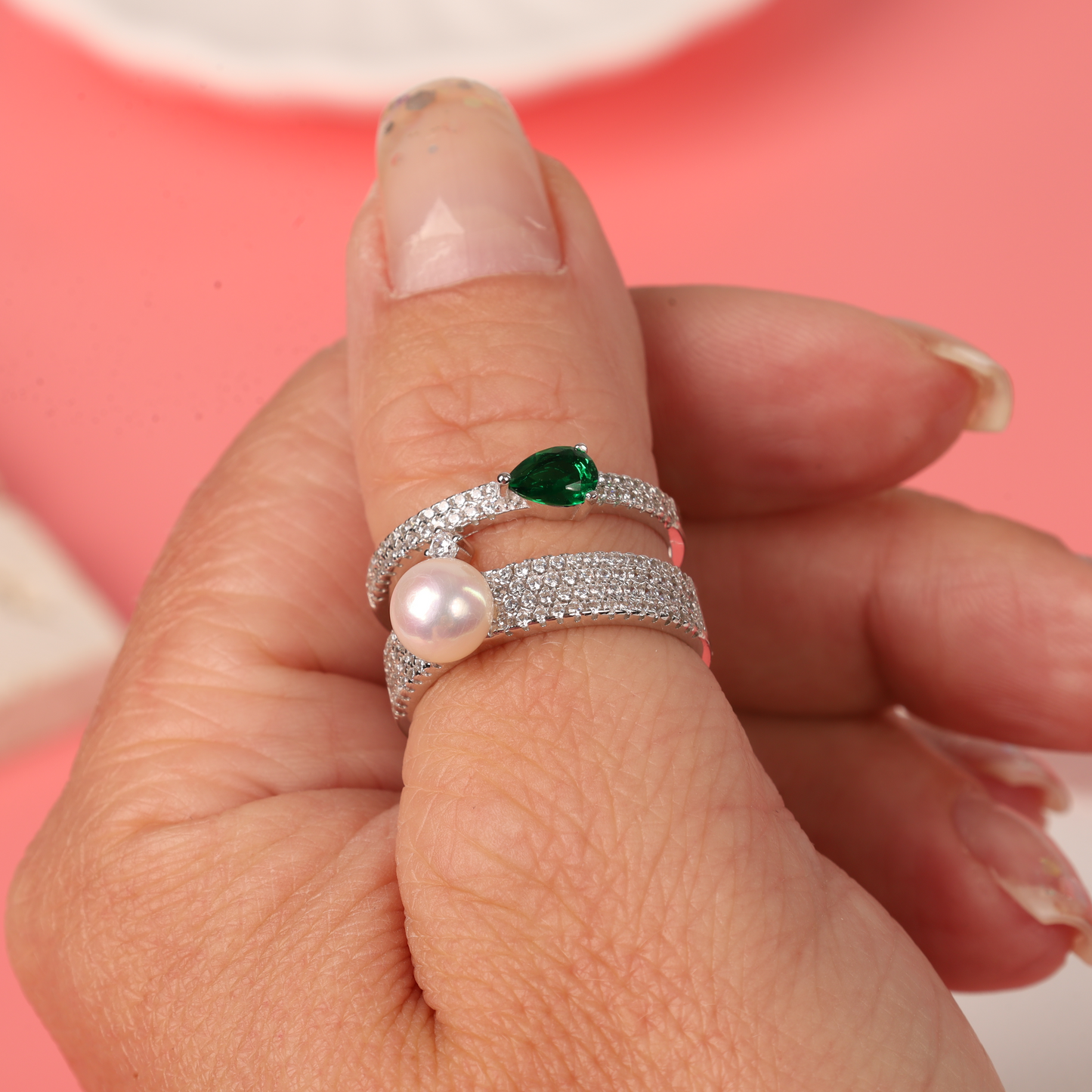 A hand adorned with the Mia Ishaaq Green Cubic Zirconia Pearl Ring, set against a soft pink background.