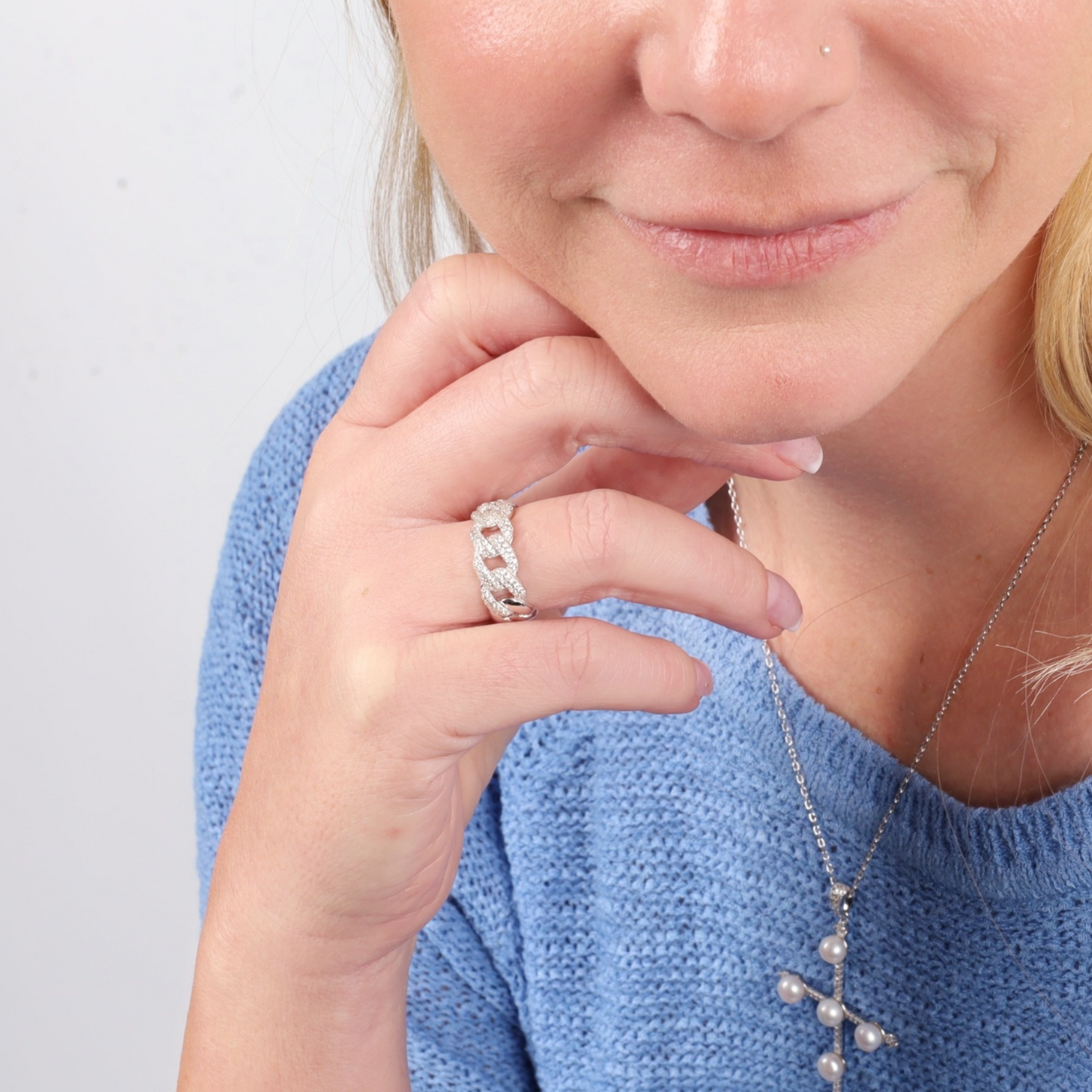 A woman in a blue sweater showcasing a Mia Ishaaq Cuban Link Chain Ring and a necklace with a cross pendant.