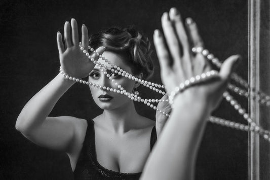 Model holding pearl necklace around her hands while looking into a mirror - Mia Ishaaq