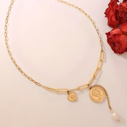 The Pearl & Coin Charm Link Necklace by Mia Ishaaq, featuring 18K gold plating with pearl and coin charm accents, is beautifully showcased alongside red dried flowers on a white background.