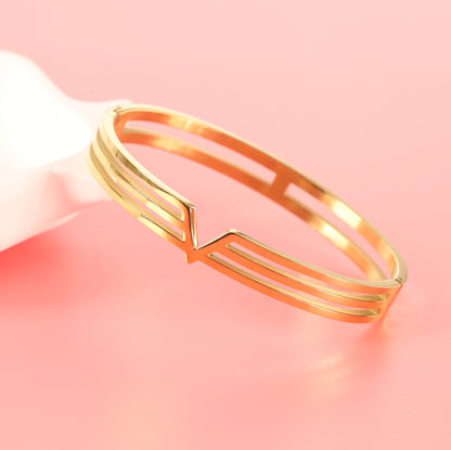 Mia Ishaaq Gold V Line Harmony Bangle Bracelet in 18k PVD Gold with a minimalist V-shaped design, showcased on a pink background for elegant versatility.