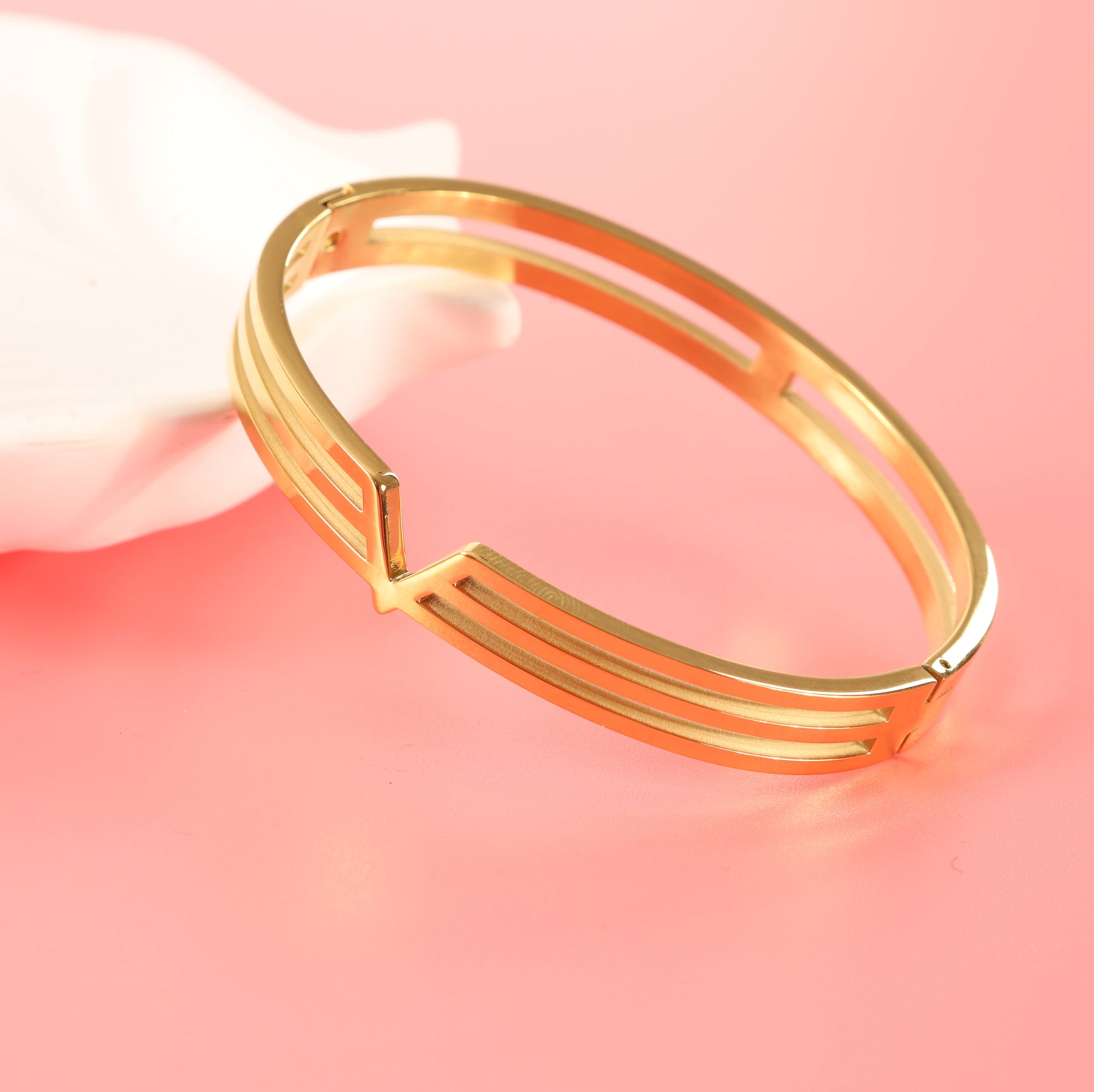 A sleek Gold V Line Harmony Bangle Bracelet by Mia Ishaaq rests on a soft pink surface.