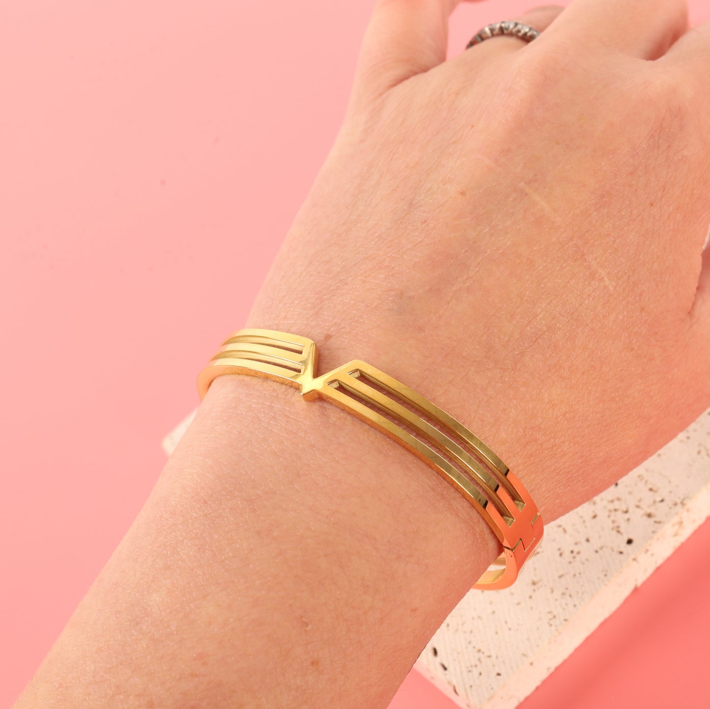 An elegant hand showcases the Mia Ishaaq Gold V Line Harmony Bangle Bracelet, featuring a striking angular and geometric design.