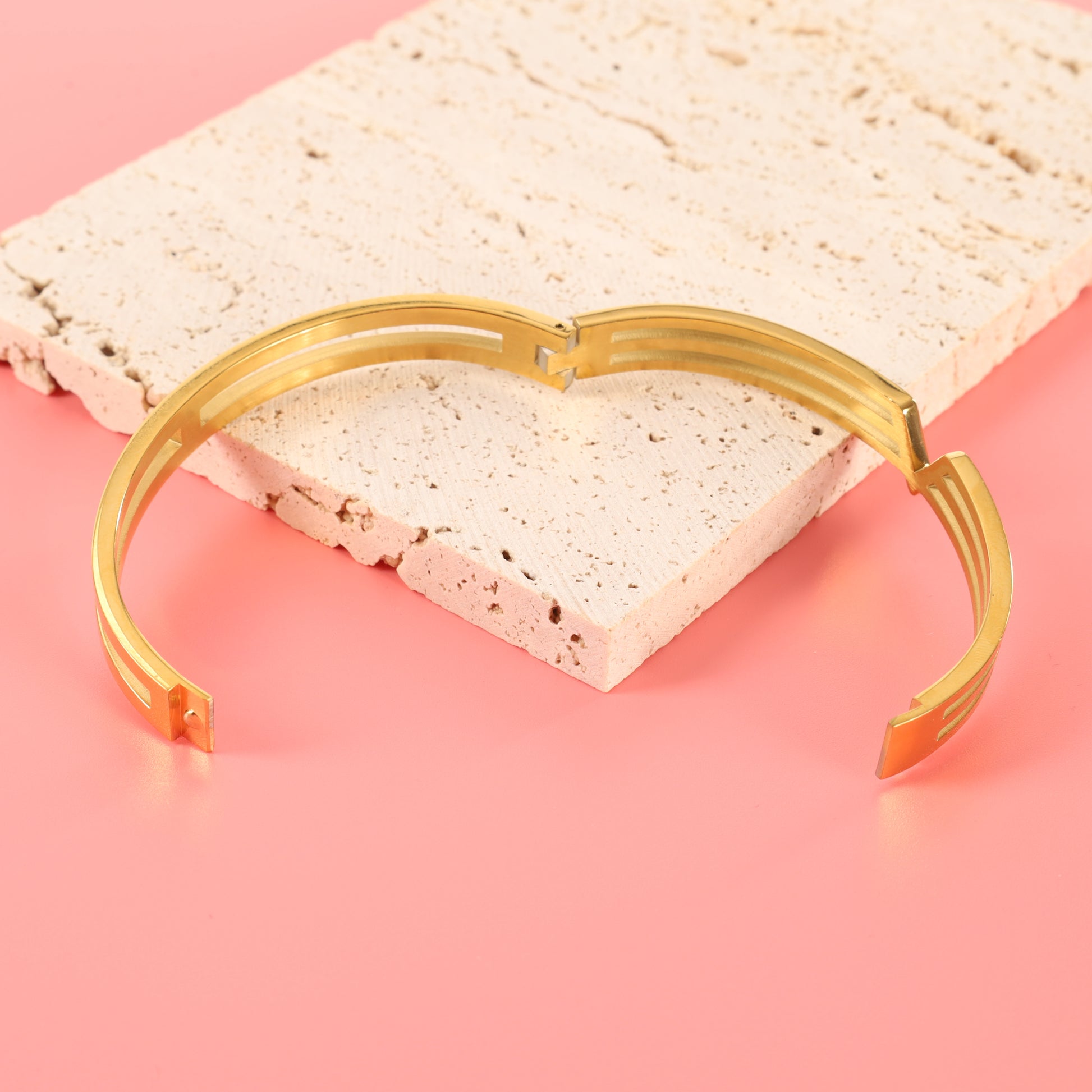 Mia Ishaaq Gold V Line Harmony Bangle Bracelet elegantly displayed on a stone slab against a pink backdrop, capturing the essence of minimalist jewellery.