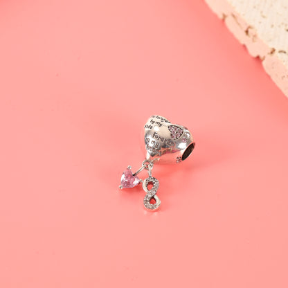 Heart-shaped dog memorial charm with pink cubic zirconia paw print and winged dog engraving, laying on a pink background - Mia Ishaaq