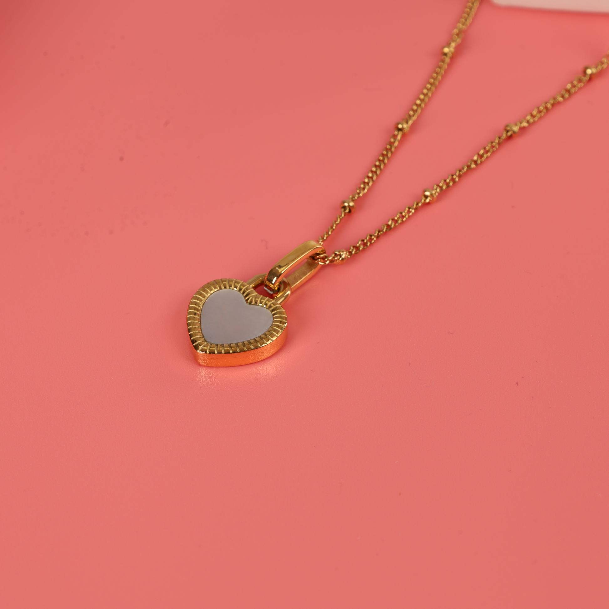 Close up of the Gold water-resistant reversible enamel heart pendant beaded chain necklace on a pink background - Mia Ishaaq