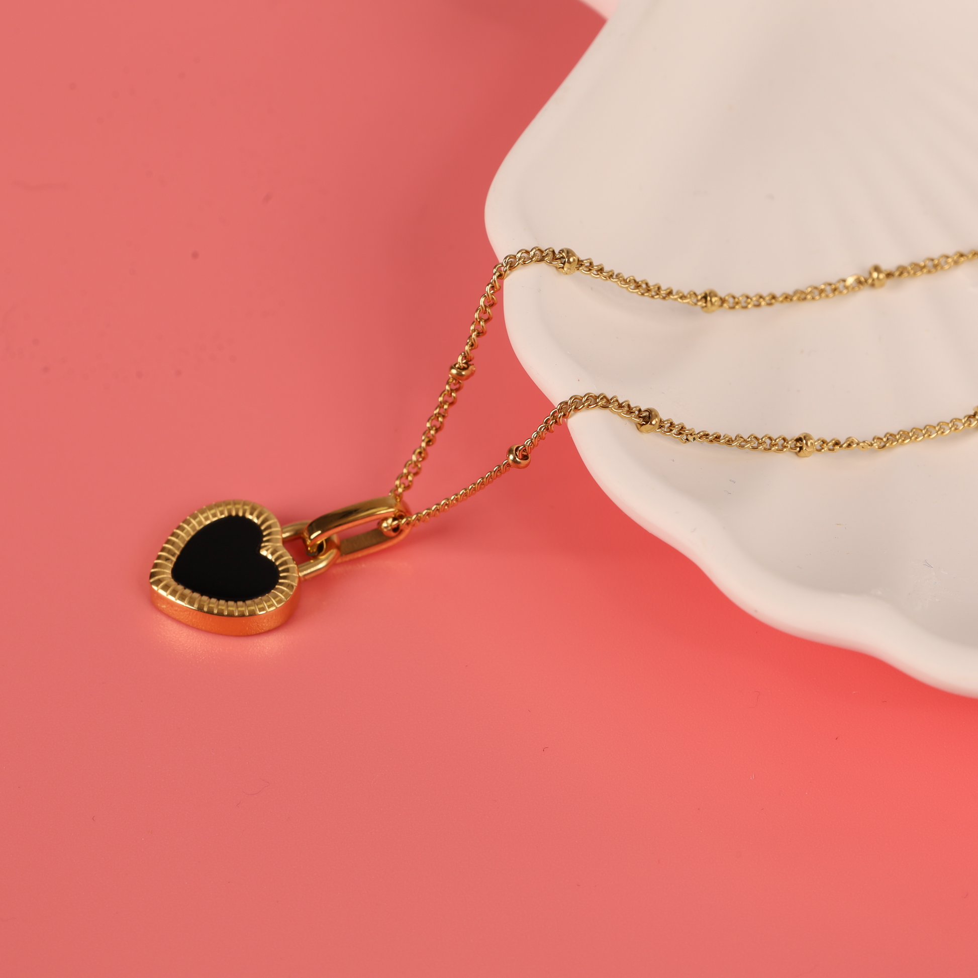 Gold water-resistant reversible enamel heart pendant beaded chain necklace placed over a white ceramic bowl on a pink background - Mia Ishaaq