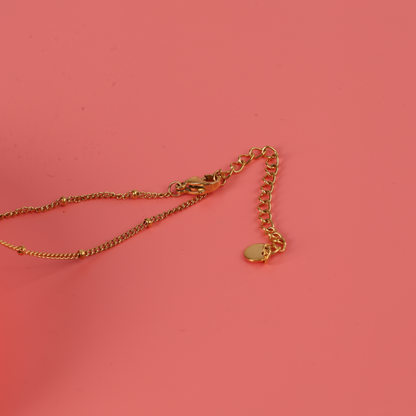 The Enamel Heart Reversible Necklace by Mia Ishaaq® is crafted from 18k gold and features a versatile heart pendant set against a coral pink background.