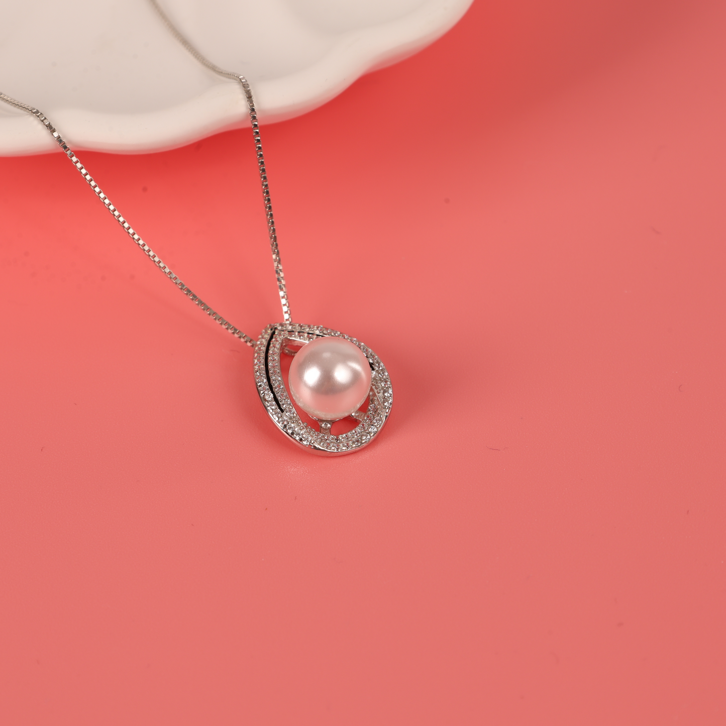 The Pearl Pendant Crystal Necklace by Mia Ishaaq, featuring a lustrous pearl, is elegantly displayed on a pink surface, accentuating its sophisticated design.