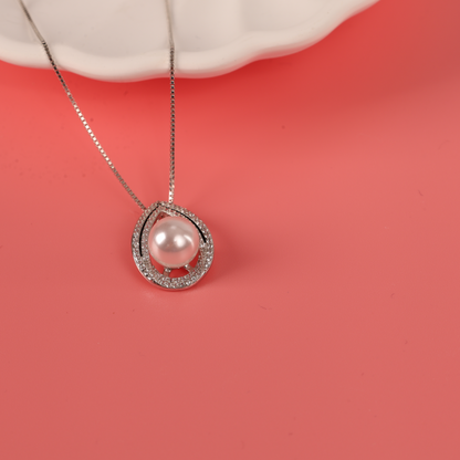 The Pearl Pendant Crystal Necklace by Mia Ishaaq showcases a captivating pearl pendant with gemstone accents, gracefully set against a coral pink backdrop.