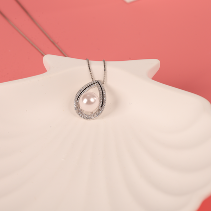 A Pearl Pendant Crystal Necklace by Mia Ishaaq rests elegantly on a white seashell against a soft pink background.