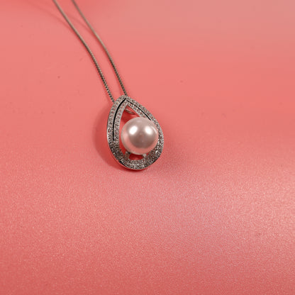 The Pearl Pendant Crystal Necklace by Mia Ishaaq stunningly features a teardrop-shaped diamond outline, elegantly suspended on a chain against a soft pink background.