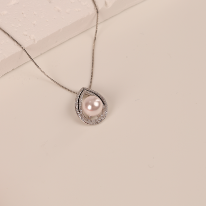 The Pearl Pendant Crystal Necklace by Mia Ishaaq features an elegant geometric design, highlighted by a stunning pearl pendant and diamond accents, gracefully displayed on a light-colored surface.