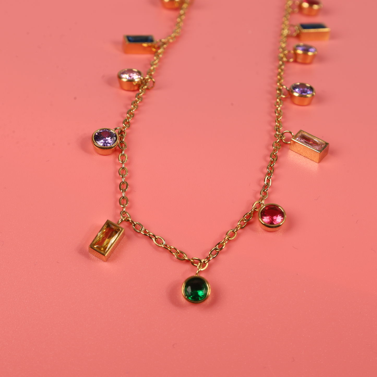 The *Mia Ishaaq® Multicoloured Gemstone Pendant Necklace*, designed with hypoallergenic 18k gold plating, shines brilliantly against a pink background.