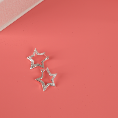 The Mia Ishaaq Sparkly Star Huggie Hoop Earrings showcase a stunning array of rhinestones set in luxurious 925 sterling silver, artfully aligned on a pink surface.