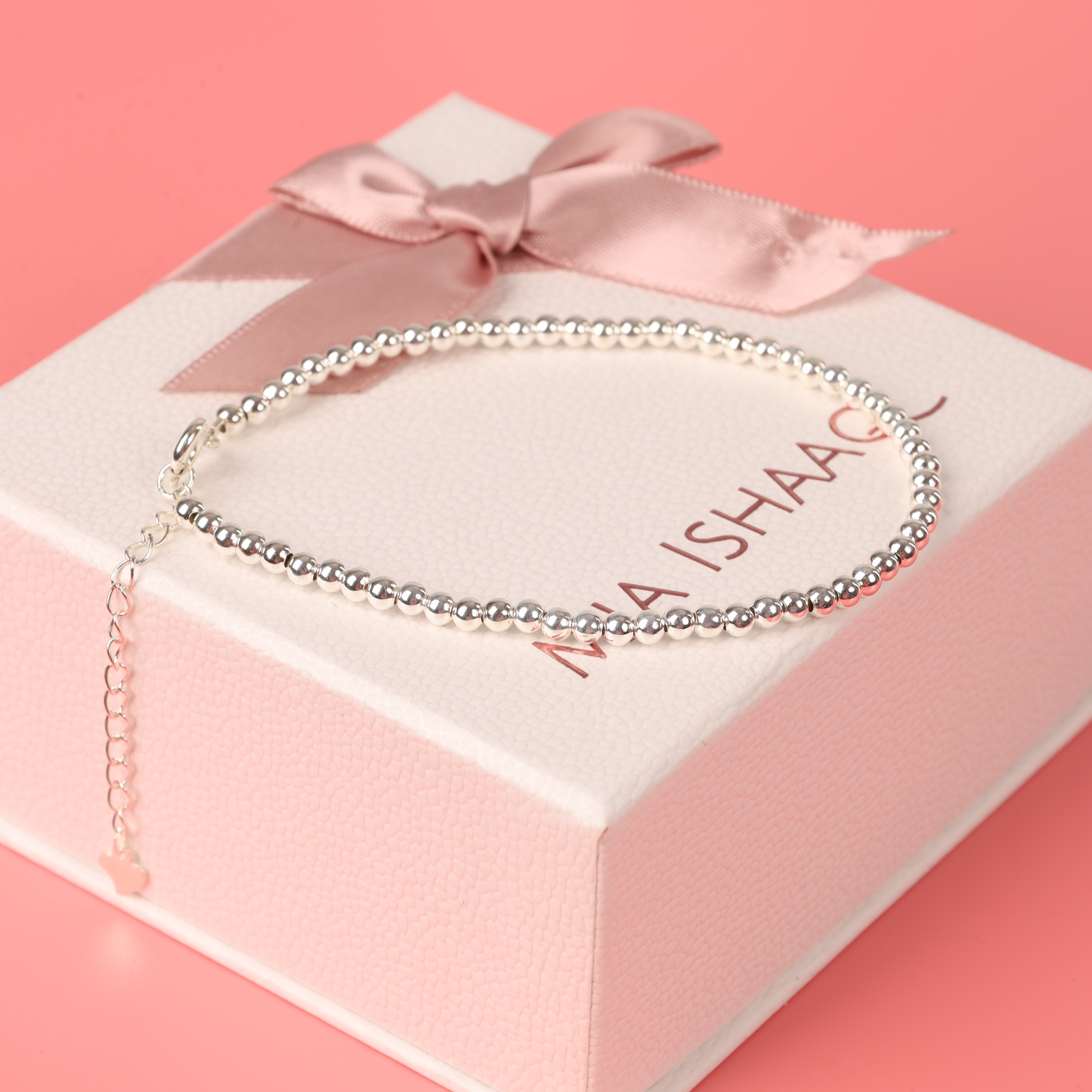 The Sterling Silver Beaded Bracelet by Mia Ishaaq rests elegantly on a pink gift box adorned with a satin bow.