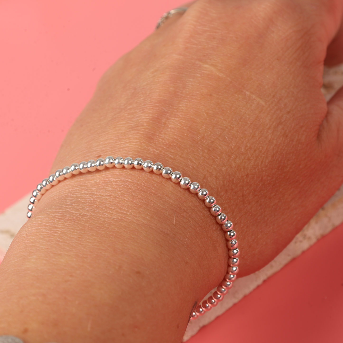 A hand wearing the Mia Ishaaq Sterling Silver Beaded Bracelet against a pink background.