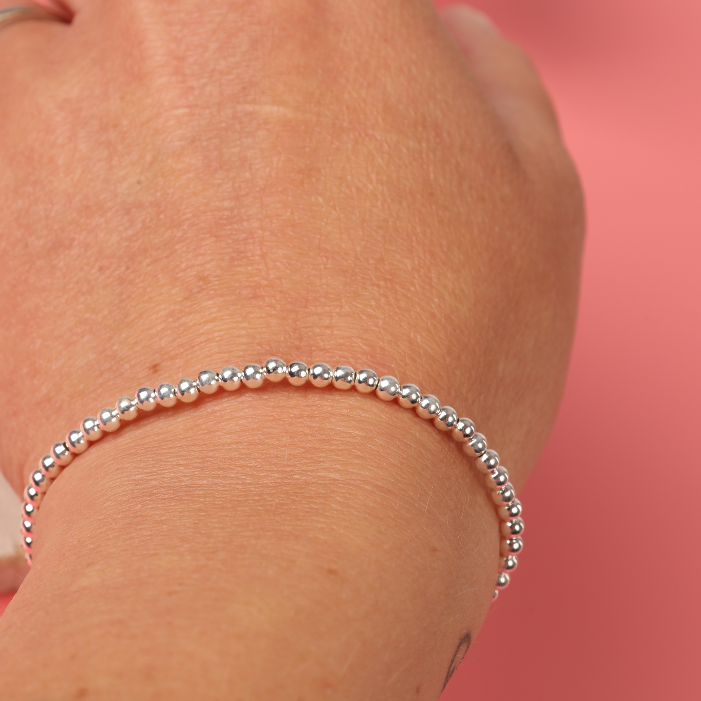 A hand elegantly displays the Sterling Silver Beaded Bracelet by Mia Ishaaq against a pink background, highlighting its minimalist design.