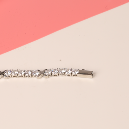 A Gemma XO Cross Love Bracelet - Silver by Mia Ishaaq is elegantly displayed on a two-toned pink and cream background, featuring exquisite 18k white gold plating.