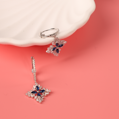 Mia Ishaaq's Blue Spinel CZ Earrings elegantly feature a floral design with blue and black gemstones set in 925 Sterling Silver, beautifully showcased on a white dish against a pink background.