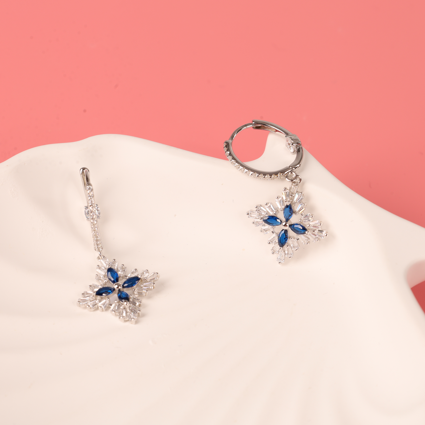 Mia Ishaaq's Blue Spinel CZ Earrings, featuring gemstone flowers on a white shell set in 925 sterling silver, displayed against a pink background.