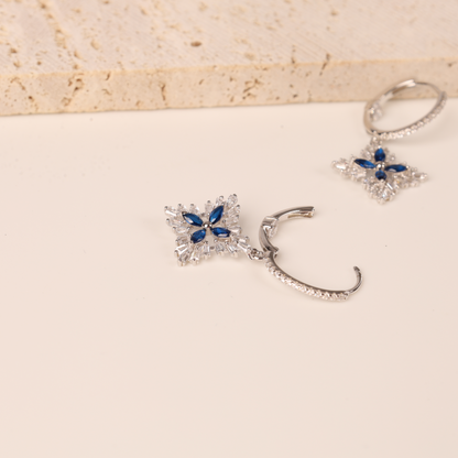 The Blue Spinel CZ Earrings by Mia Ishaaq are stunning star-shaped earrings featuring dazzling blue gems and intricate silver details, beautifully crafted with 925 Sterling Silver, set on a light surface.