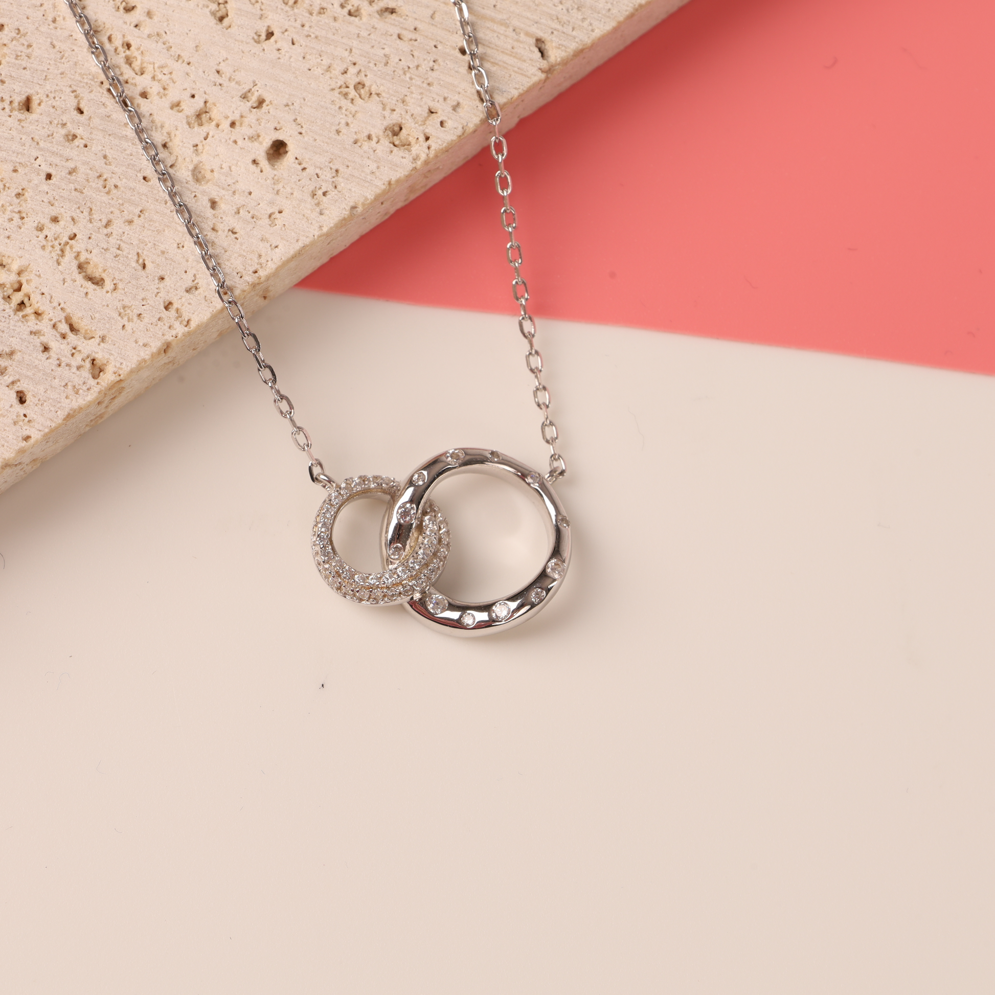 Top view of 925 sterling silver interlocking circle eternity friendship necklace on a half white half pink background - Mia Ishaaq