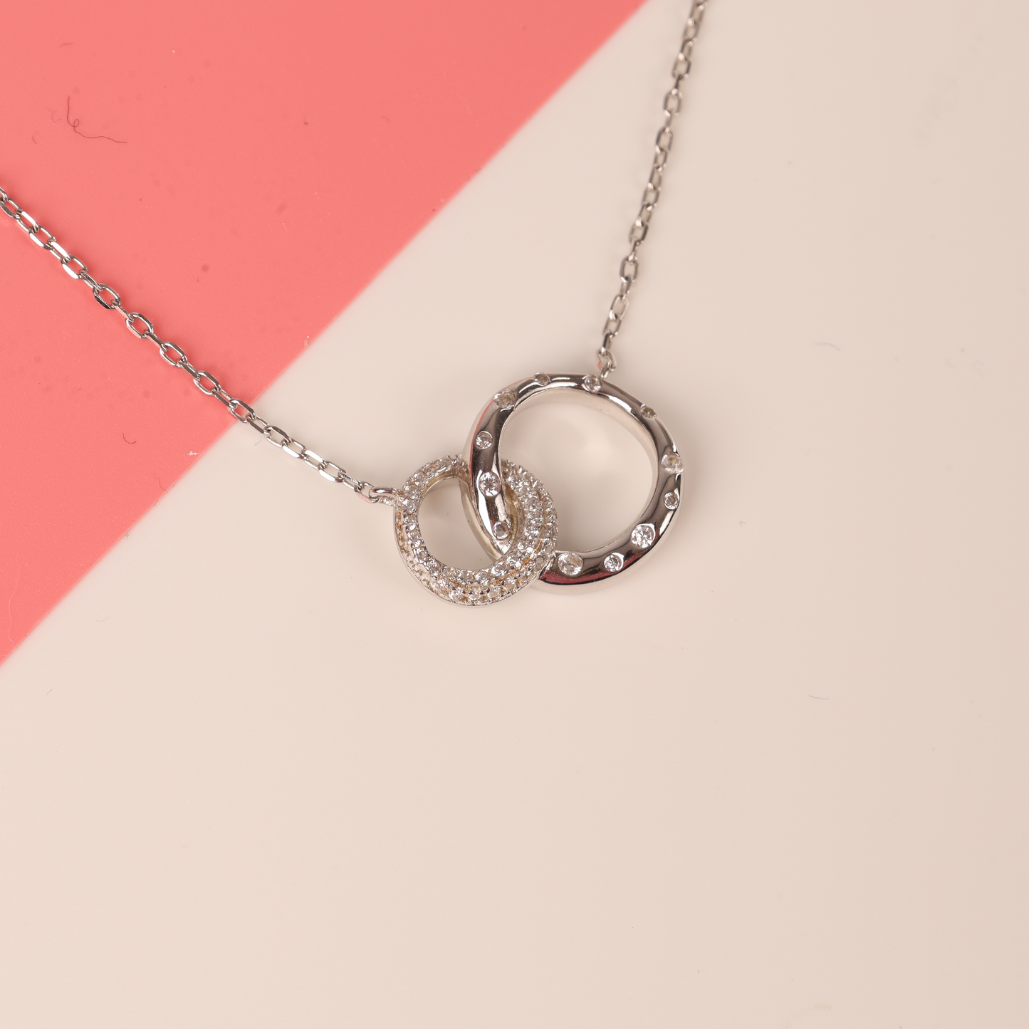 Close up top view of the 925 sterling silver interlocking circle eternity friendship necklace on a half white half pink background - Mia Ishaaq