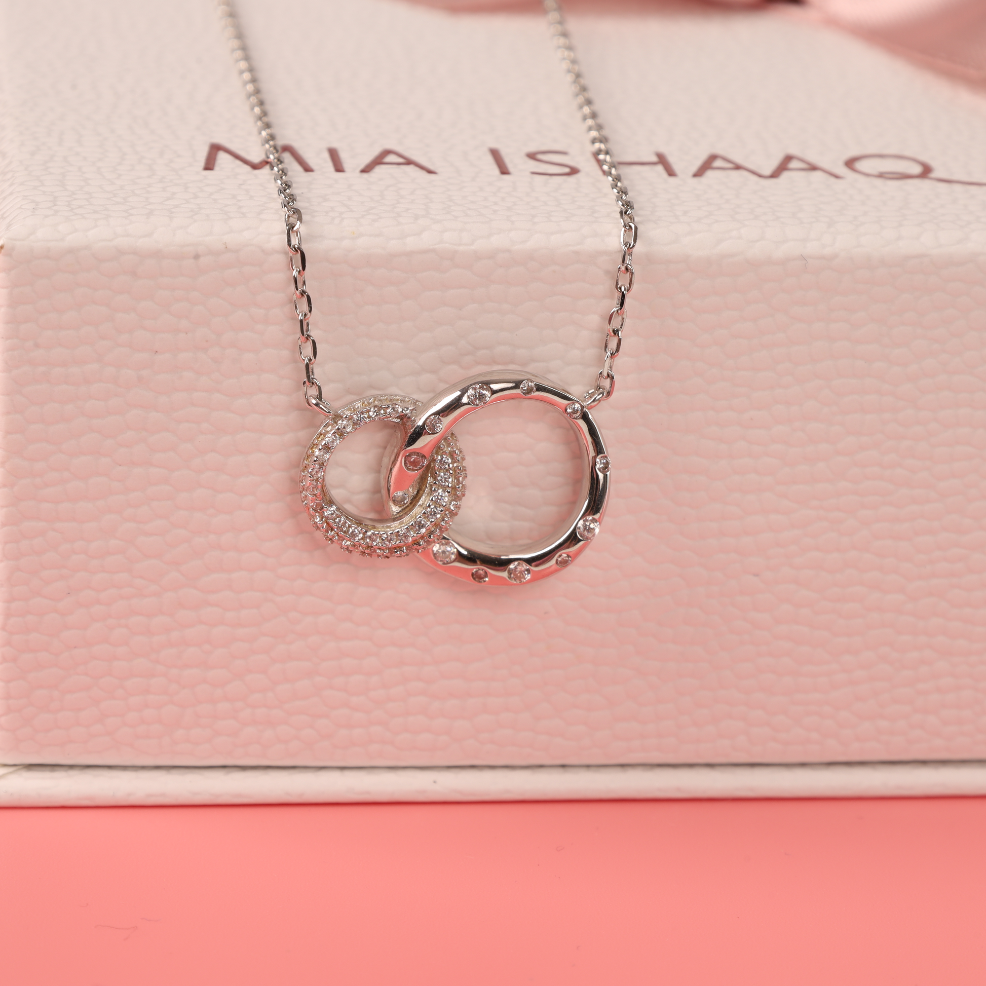 925 sterling silver interlocking circle eternity friendship necklace hanging over the edge of our signature gift boxes and a pink background - Mia Ishaaq