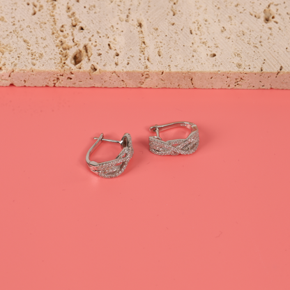 A top view of the Twilight Criss-Cross Earrings on a pink background, with a natural colour prop underneath, showcasing the earrings' unique shape and texture - Mia Ishaaq