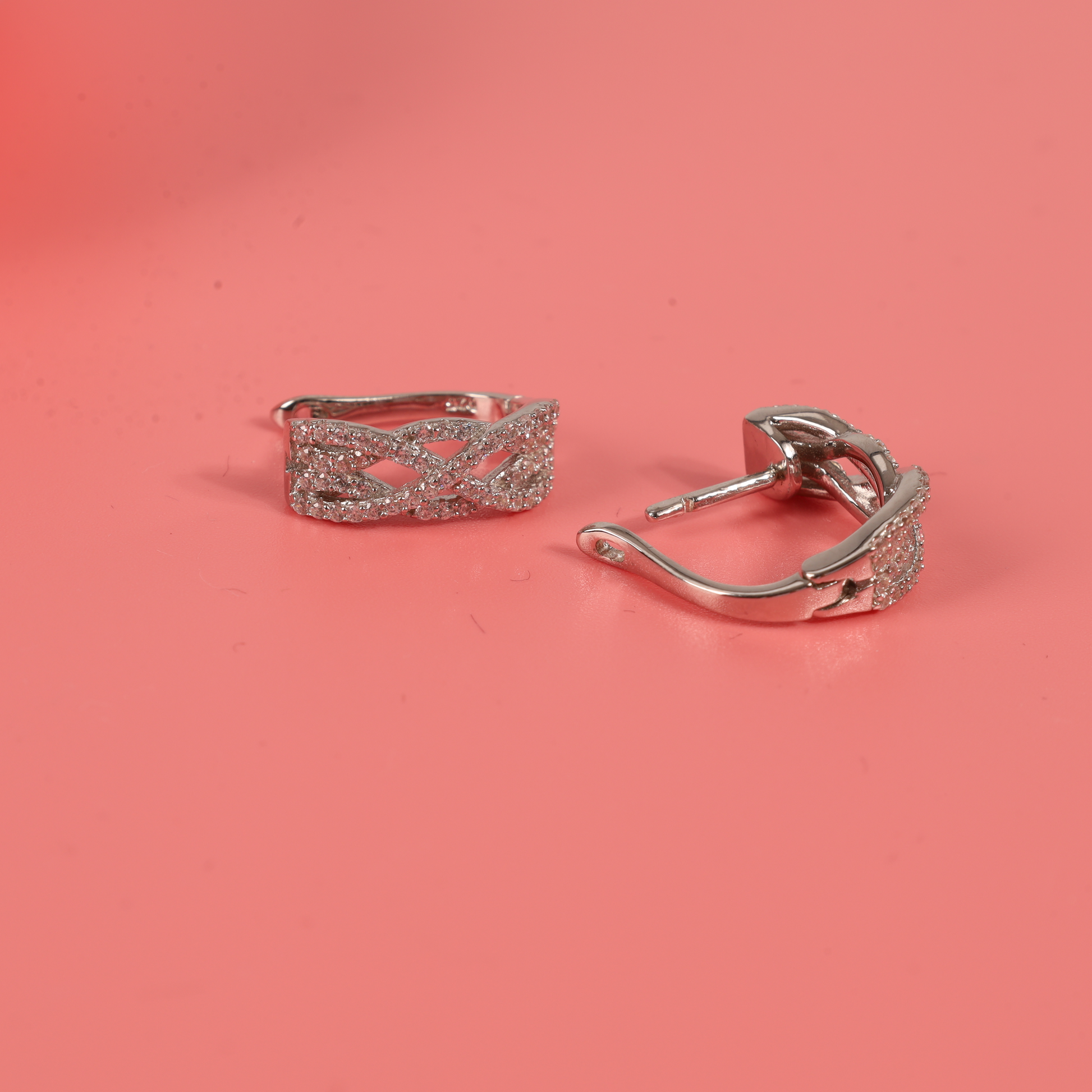 The Twilight Criss-Cross Earrings displayed on a pink background, with one earring slightly opened, revealing the beautiful craftsmanship and intricate details - Mia Ishaaq