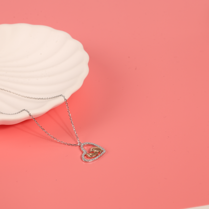 Sterling Silver Cubic Zirconia Mothers Love Heart Pendant with baby footprints necklace placed over a white ceramic bowl on a pink backdrop - Mia Ishaaq