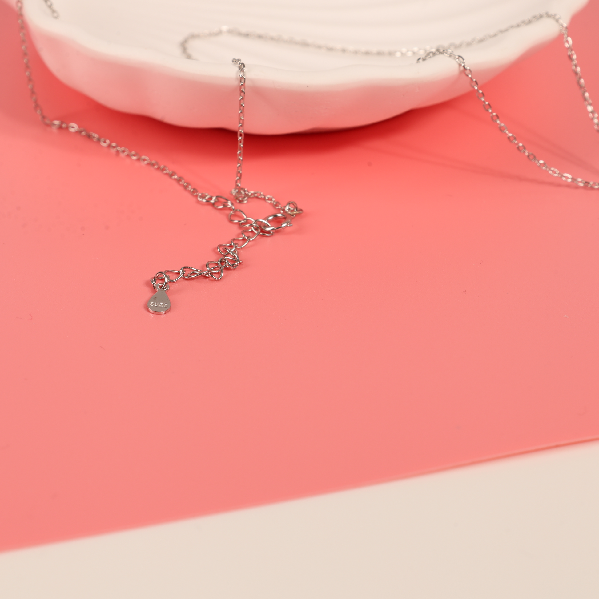 Detail of a chain of the Sterling Silver Cubic Zirconia Mothers Love Heart Pendant with baby footprints necklace on a pink background - Mia Ishaaq