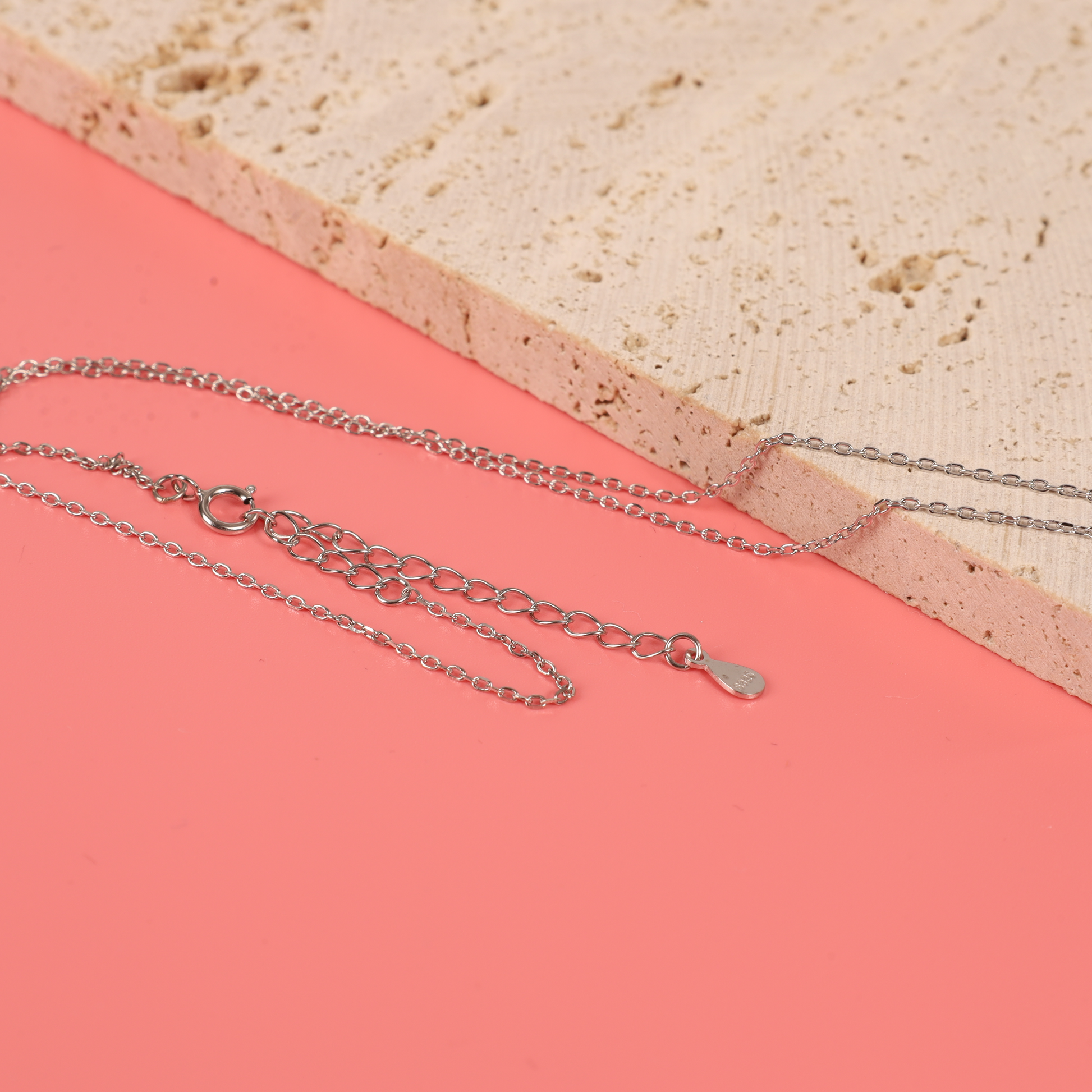 Detail of the clasp and extension chain of the Sterling Silver Cubic Zirconia Mothers Love Heart Pendant with baby footprints necklace on the pink background - Mia Ishaaq