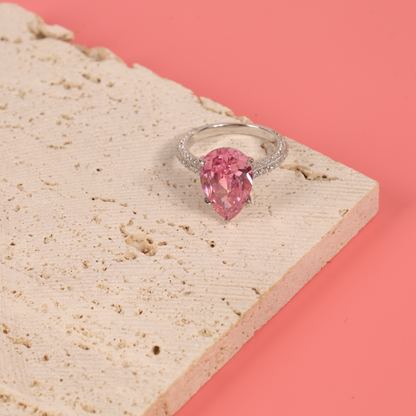 The Blush Drop Elegance Ring positioned on a pastel pink background, accented by elegant white decorative stones for a chic display - Mia Ishaaq