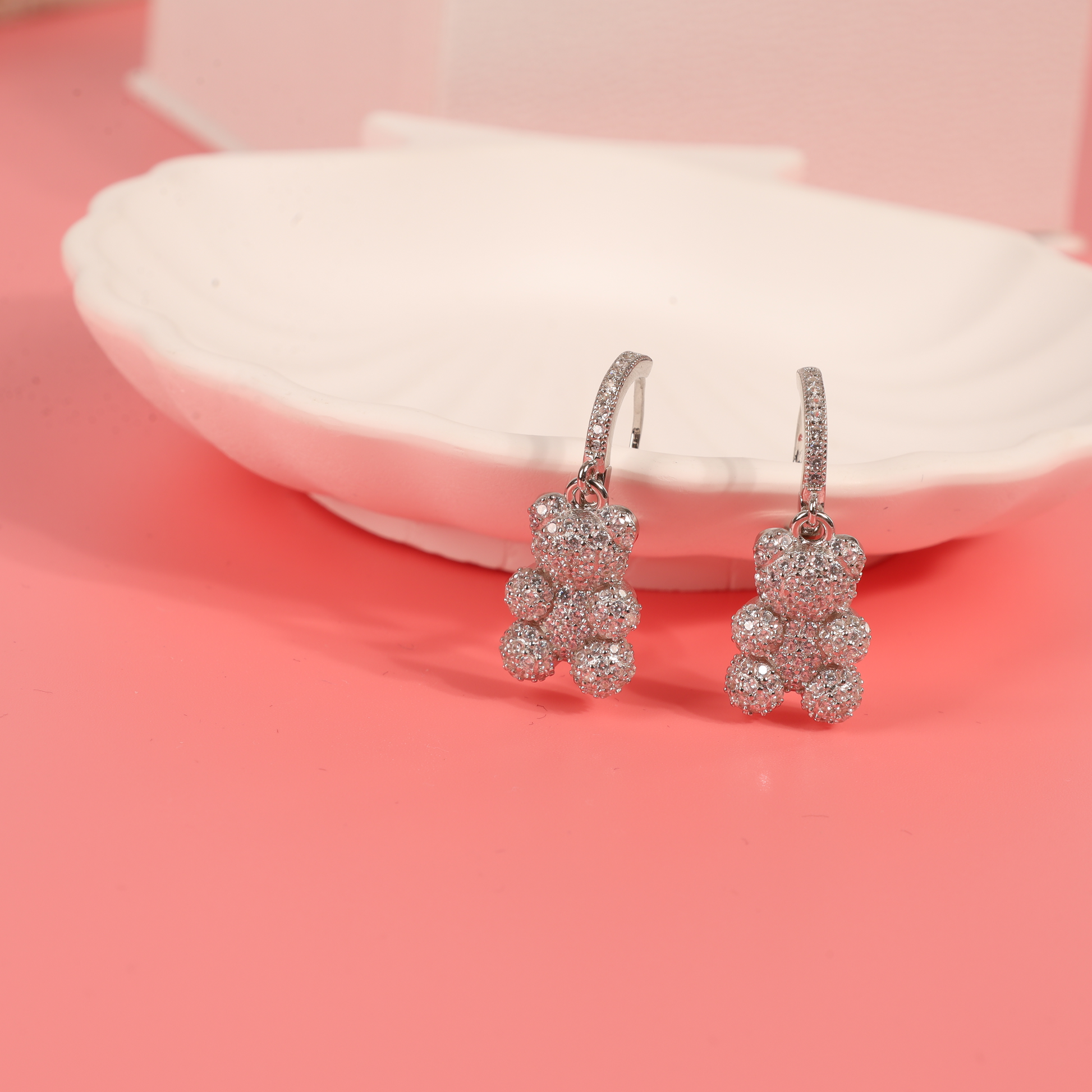 Side view of the teddy bear dangle earrings on a pink background, showcasing the flat back design and hoop closure for comfortable wear - Mia Ishaaq