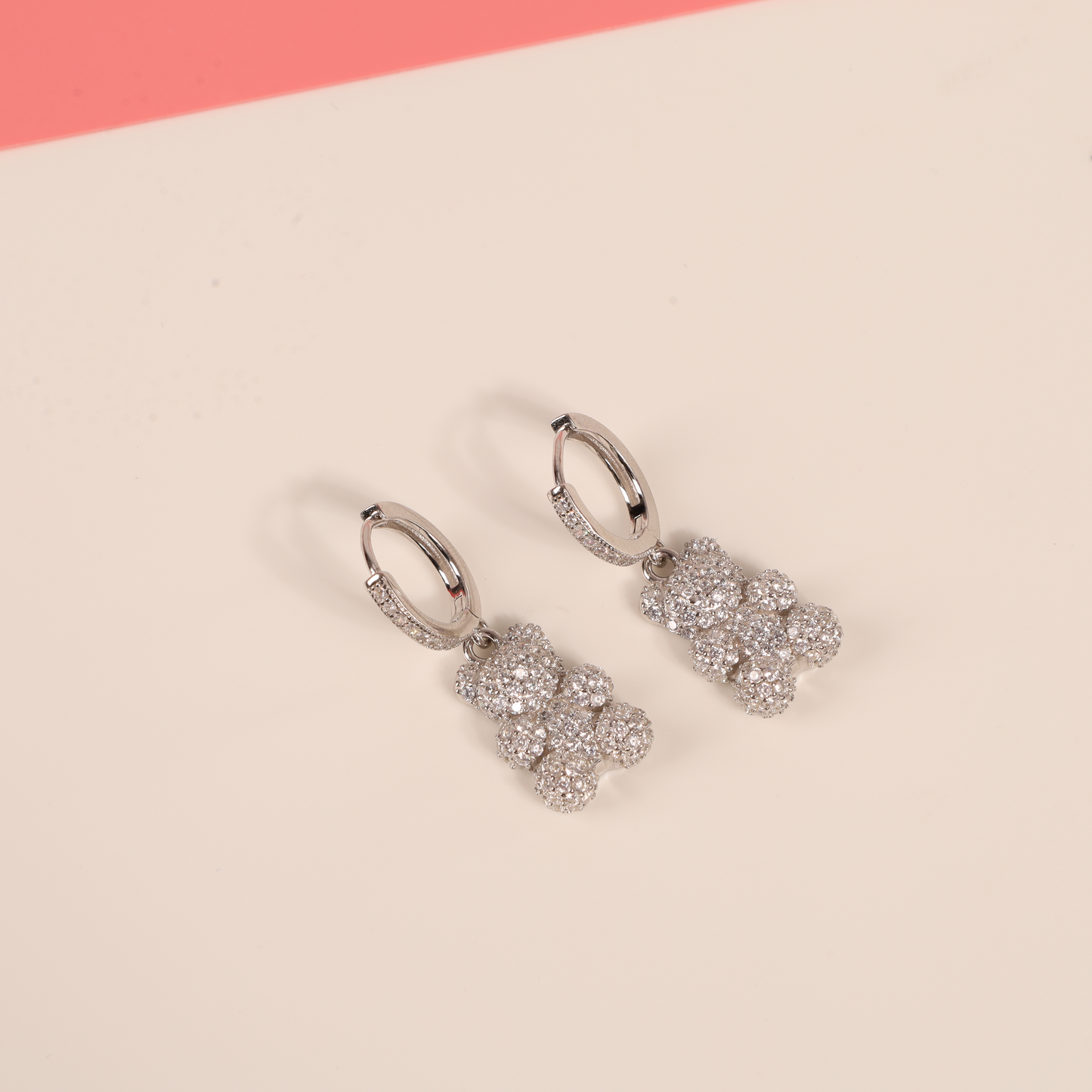 Close-up of teddy bear dangle earrings on a white background with pink backdrop, highlighting the cubic zirconia detailing and whimsical design - Mia Ishaaq