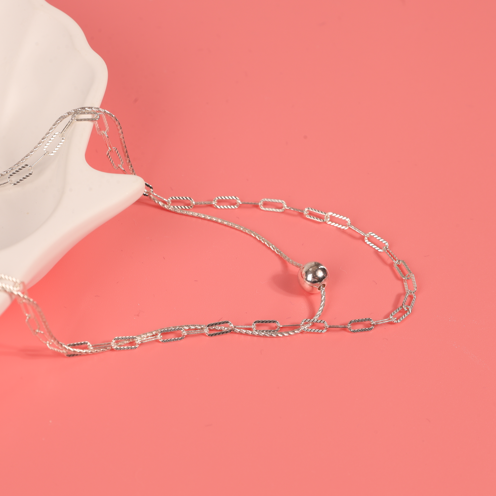 The layered necklace elegantly arranged in a white ceramic shell-shaped bowl against a pink background, highlighting both chains in a soft, flattering light - Mia Ishaaq