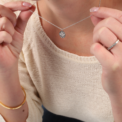 A person holds the Polaris Coin Pendant Necklace by Mia Ishaaq® in silver, styled with a cream sweater and a bracelet.