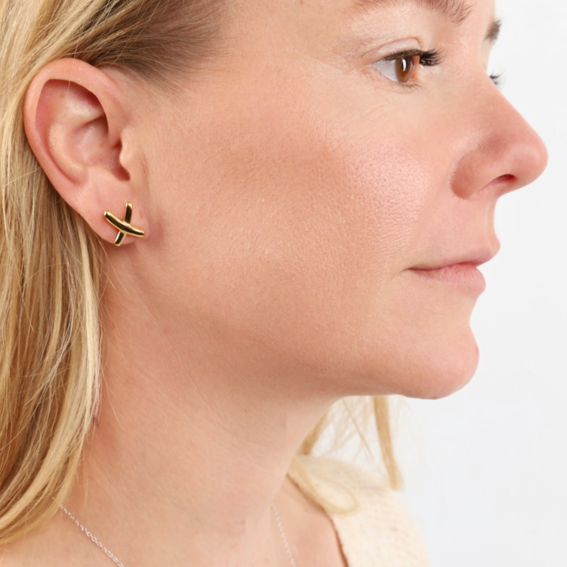 Close-up of a woman wearing the Gemma Owen Inspired XO Cross Stud Earrings by Mia Ishaaq®, featuring elegant 18k gold plating, set against a plain background.