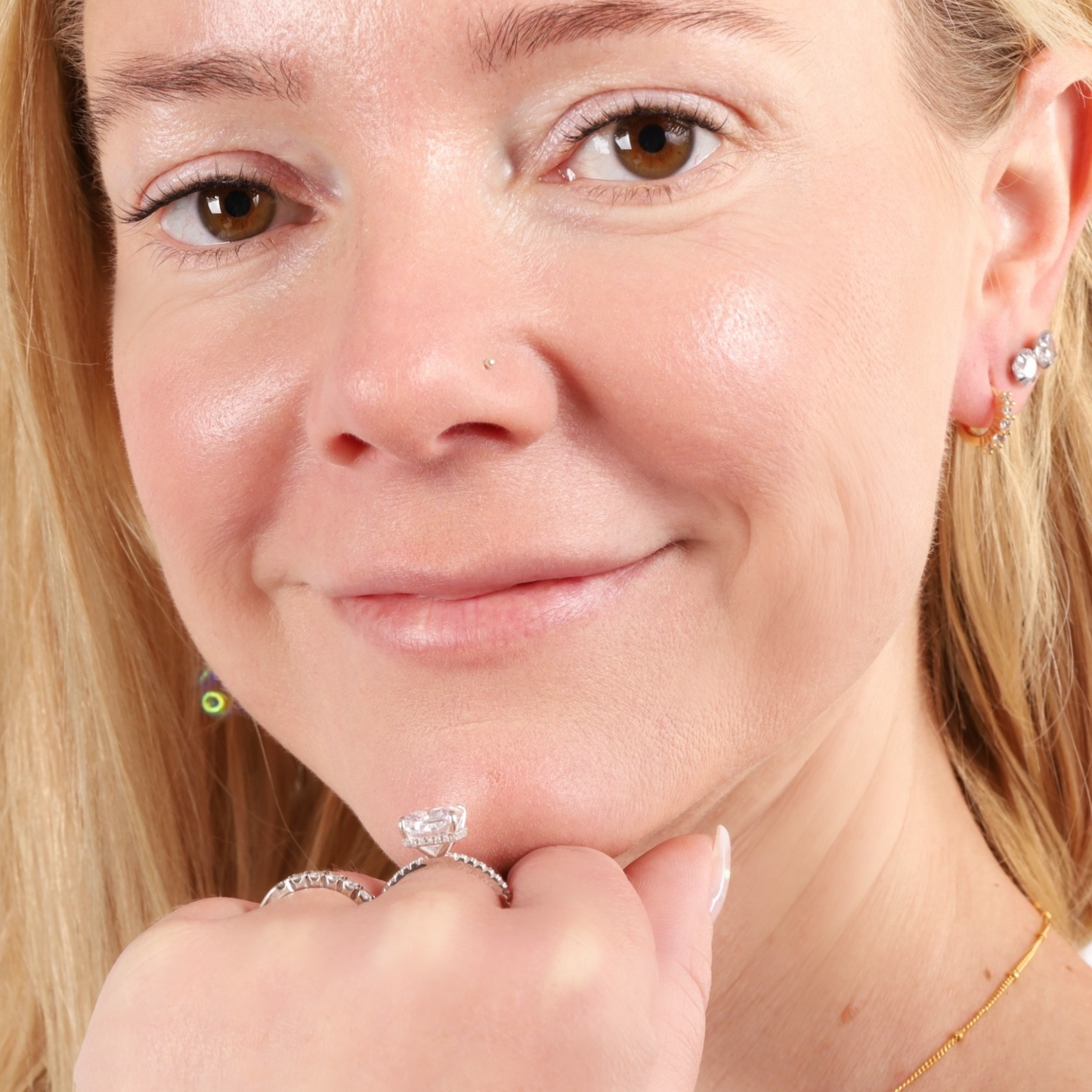 A smiling woman proudly displays a Sterling Silver Clear Radiant Ring by Mia Ishaaq on her fingers, close-up portrait.