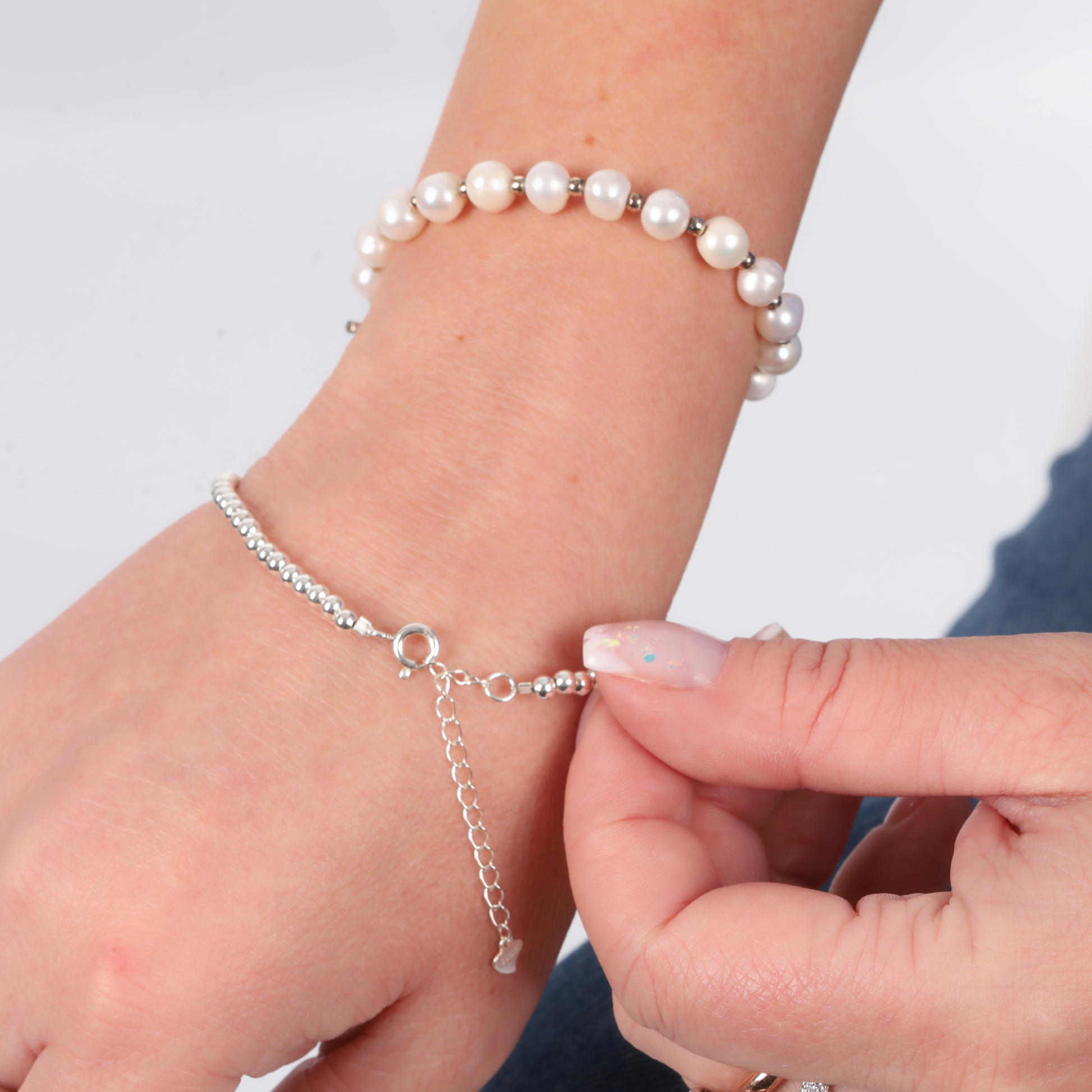 Carefully fastening a Mia Ishaaq Sterling Silver Beaded Bracelet alongside a pearl bracelet on the wrist against a white background, highlighting the elegant minimalist design that beautifully complements both pieces.