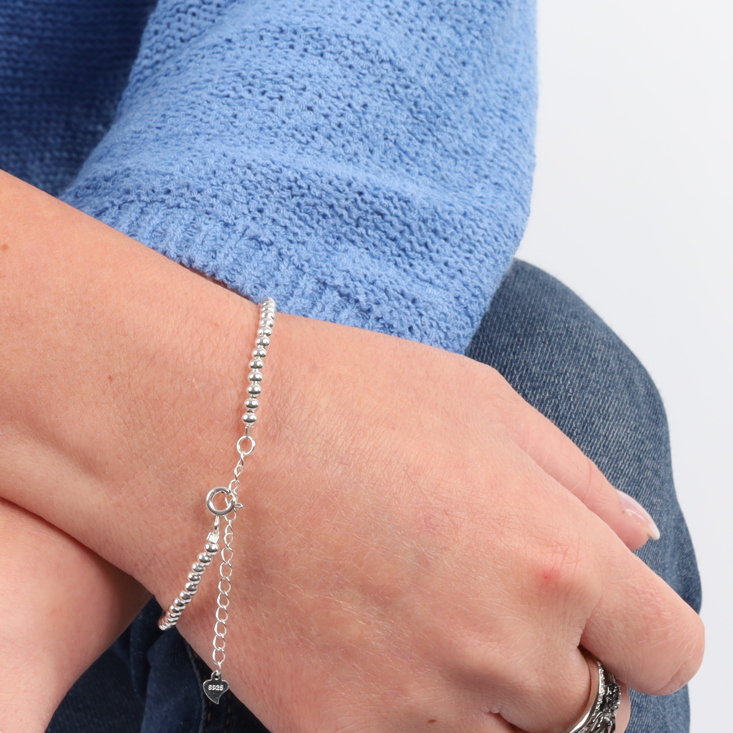 Close-up of a person wearing the Mia Ishaaq Sterling Silver Beaded Bracelet, paired with a blue knitted sweater and denim jeans.