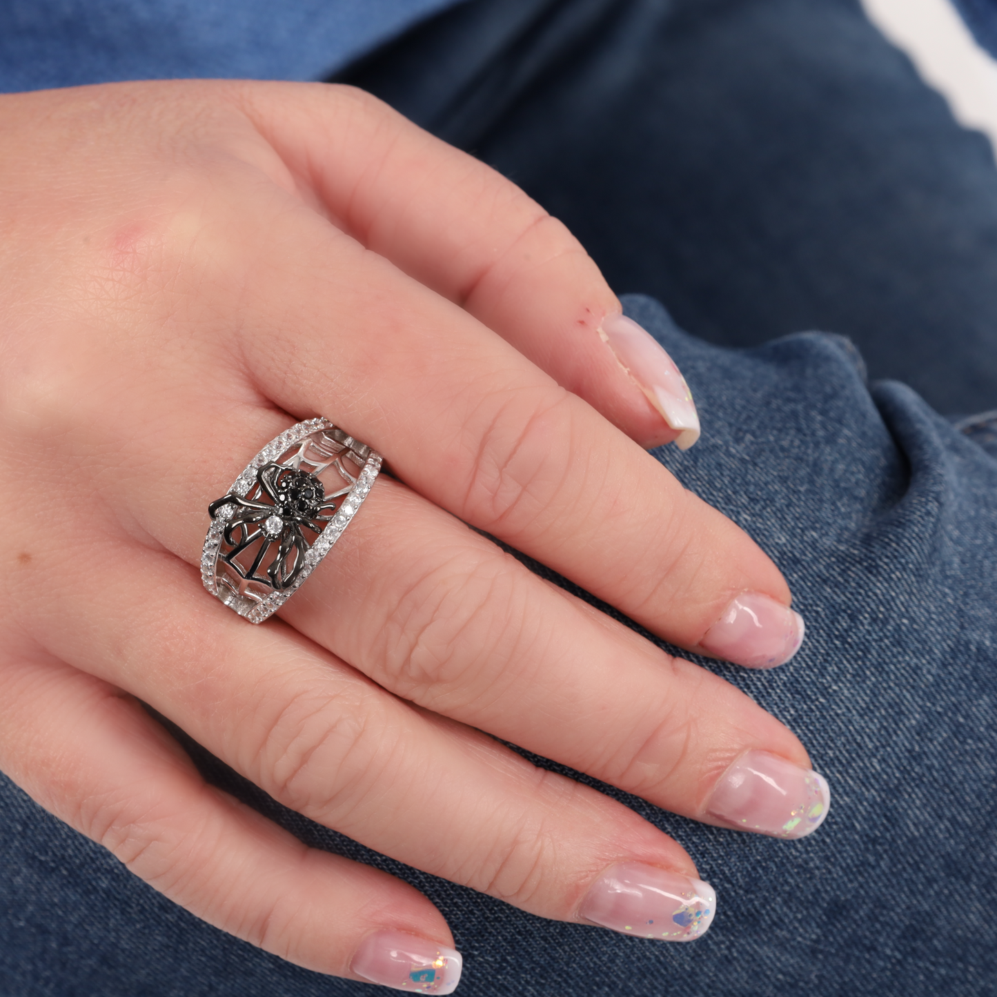 Close-up of a hand on a denim-clad knee, adorned with the intricate design of a sterling silver ring from the Halloween Earrings and Ring Set by Mia Ishaaq, perfectly complementing the allure of gothic jewelry.