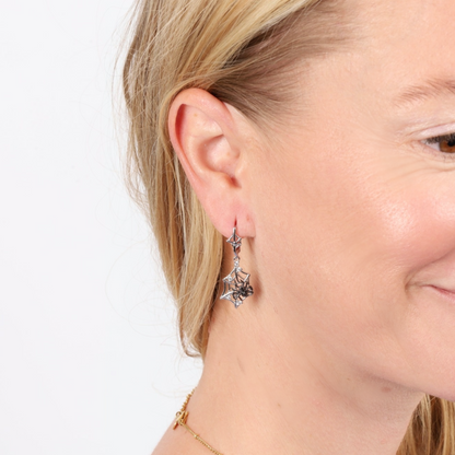 Close-up of a woman wearing earrings from the Mia Ishaaq Halloween Earrings and Ring Set, featuring sterling silver stars, with a slight smile against a white background.